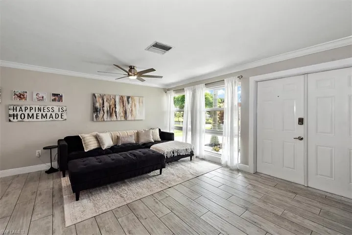 Living area with light wood-type flooring, ornamental molding, and a ceiling fan