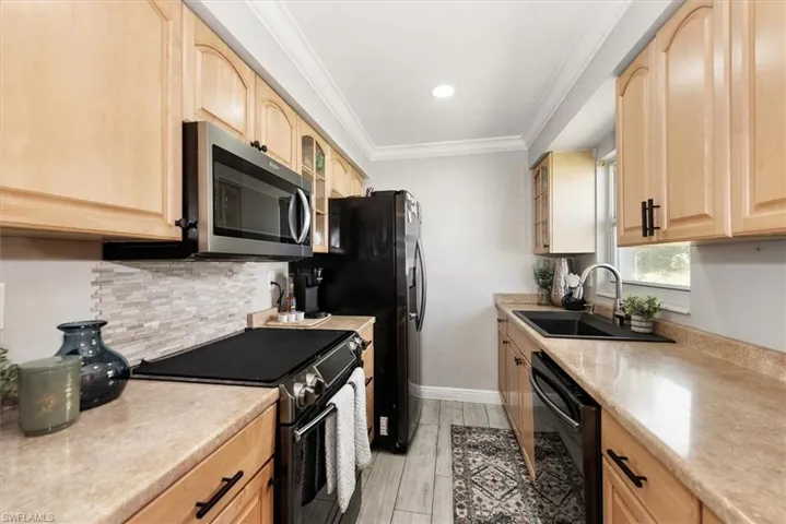 Kitchen with stainless steel appliances, glass insert cabinets, light brown cabinetry, ornamental molding, and light wood-style flooring