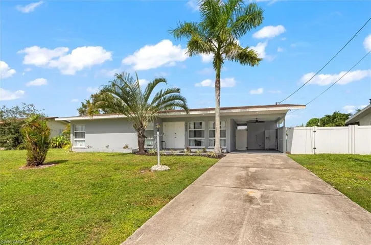 View of front of property featuring an attached carport, driveway, a front lawn, and stucco siding
