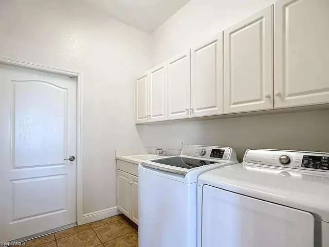Laundry area featuring washer and clothes dryer, sink, light tile floors, and cabinets