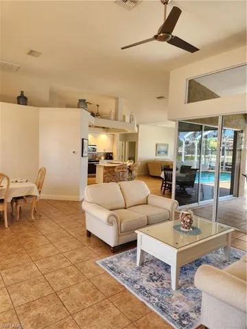 Living room featuring light tile patterned floors, visible vents, lofted ceiling, and a ceiling fan