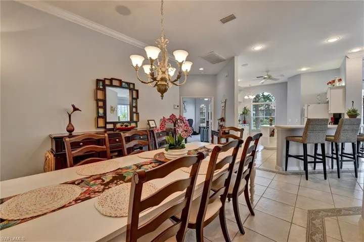 Tiled dining room featuring ceiling fan with notable chandelier and ornamental molding