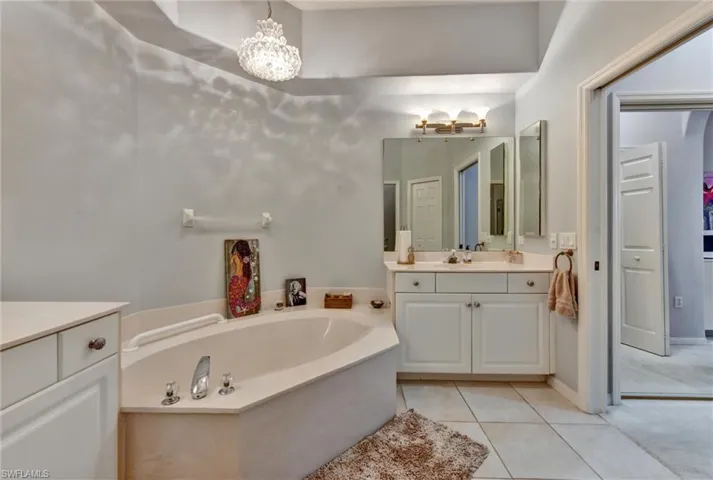 Bathroom with a notable chandelier, large vanity, tile flooring, and a bathing tub