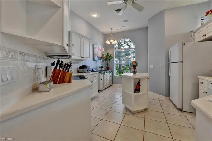 Kitchen with white fridge, ceiling fan with notable chandelier, tasteful backsplash, and white cabinetry