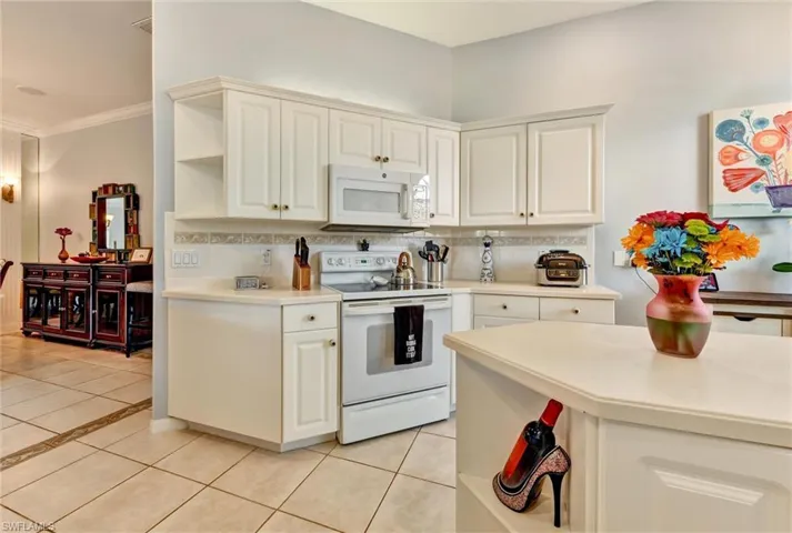 Kitchen featuring crown molding, tasteful backsplash, light tile flooring, and white appliances