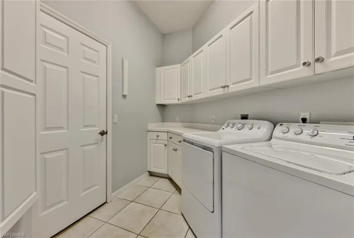 Clothes washing area with electric dryer hookup, washer and dryer, cabinets, and light tile floors
