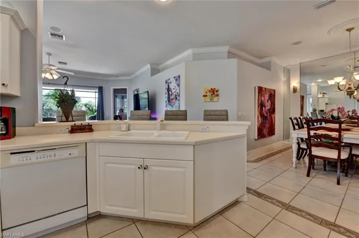 Kitchen with dishwasher, white cabinetry, light tile floors, and crown molding