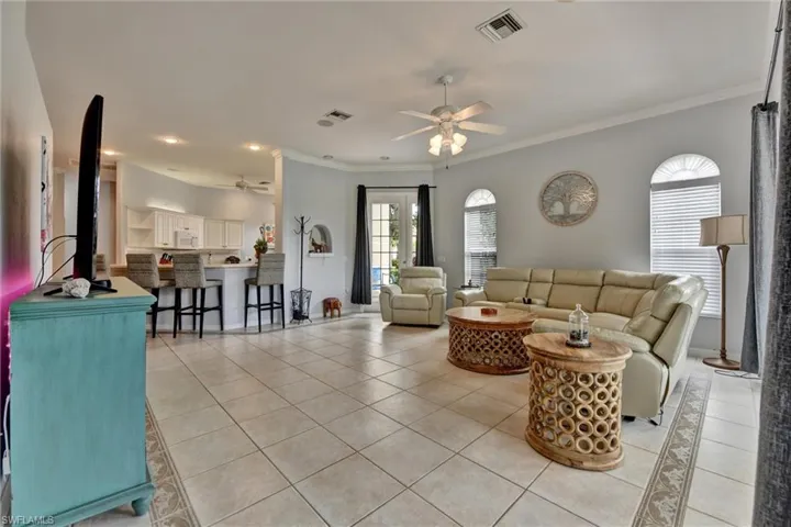 Living room with ceiling fan, ornamental molding, and light tile floors