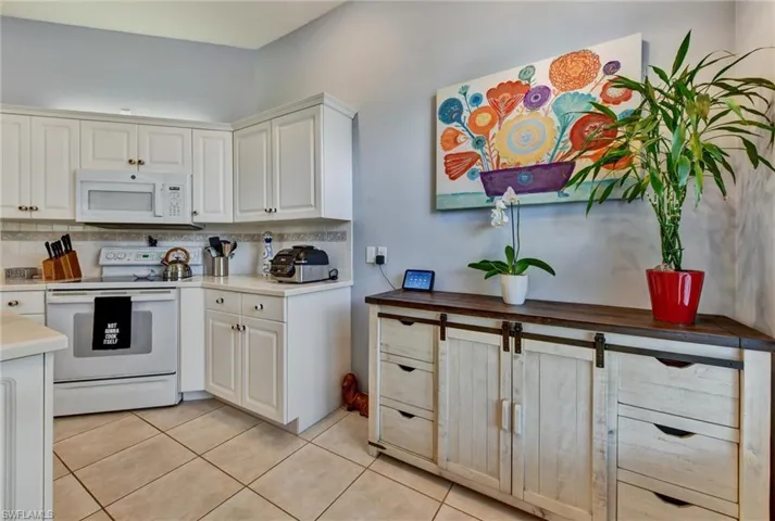 Kitchen featuring white cabinets, light tile floors, white appliances, and backsplash