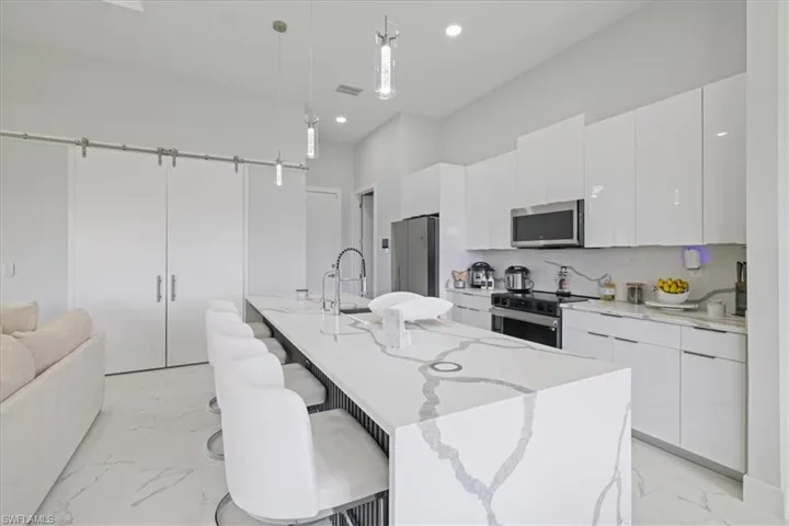 Kitchen featuring a kitchen breakfast bar, modern cabinets, pendant lighting, light marble finish floors, and white cabinets