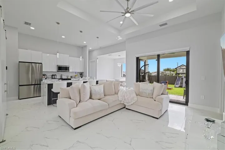 Living room featuring a raised ceiling, light marble finish floors, recessed lighting, a ceiling fan, and a towering ceiling