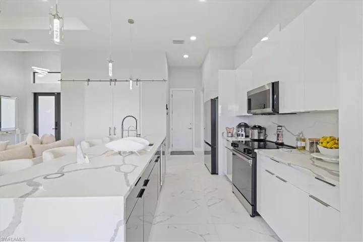 Kitchen with modern cabinets, decorative light fixtures, appliances with stainless steel finishes, light stone countertops, and white cabinets