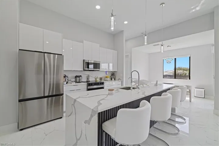Kitchen with stainless steel appliances, light marble finish floors, hanging light fixtures, a breakfast bar area, and white cabinetry