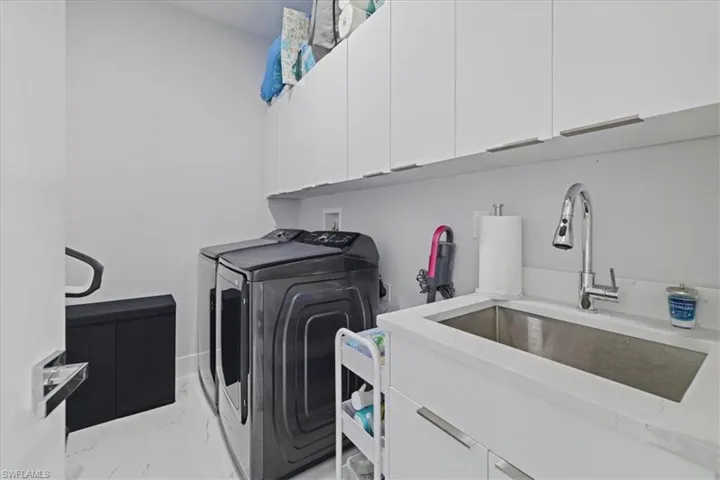 Washroom featuring light marble finish floors, cabinet space, and washing machine and dryer