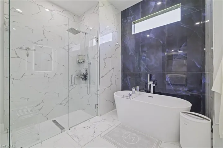 Bathroom featuring stone wall, a freestanding bath, marble tiled floors, a marble finish shower, and tile walls