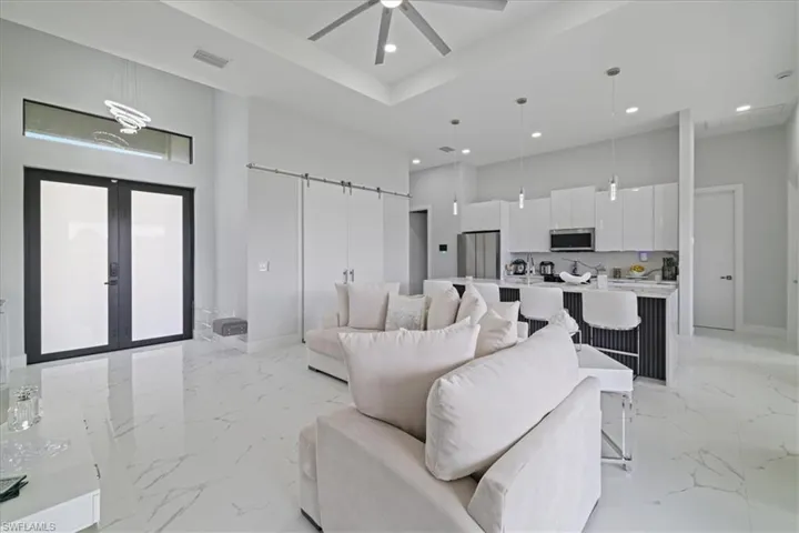 Living room featuring a barn door, light marble finish floors, french doors, a towering ceiling, and a ceiling fan