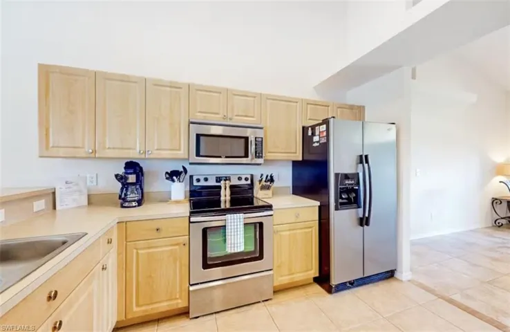 Kitchen featuring stainless steel appliances, wood-finish cabinetry, light-toned countertops, and tiled flooring