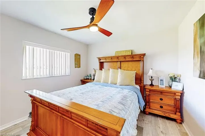 Interior room featuring wood-finish flooring, a window with vertical blinds, a ceiling fan with wooden blades and integrated lighting, and light-toned walls