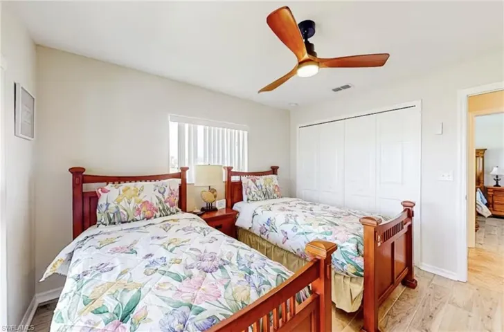 Bedroom featuring two beds with wooden frames, wood-finish flooring, a ceiling fan with integrated lighting, and a window with horizontal blinds