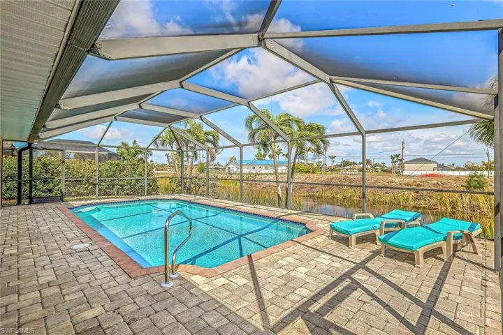 Screened-in pool area featuring a rectangular pool with integrated steps, paver decking, and a metal handrail