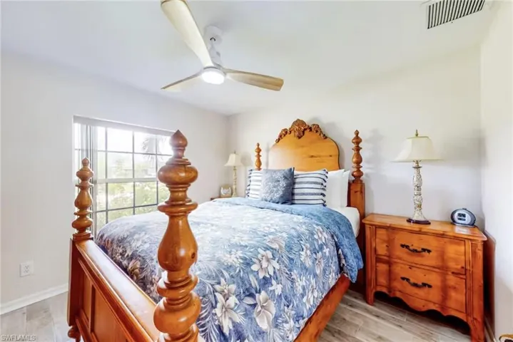 Bedroom featuring wood-finish flooring, a window with horizontal blinds, and a ceiling fan with integrated lighting