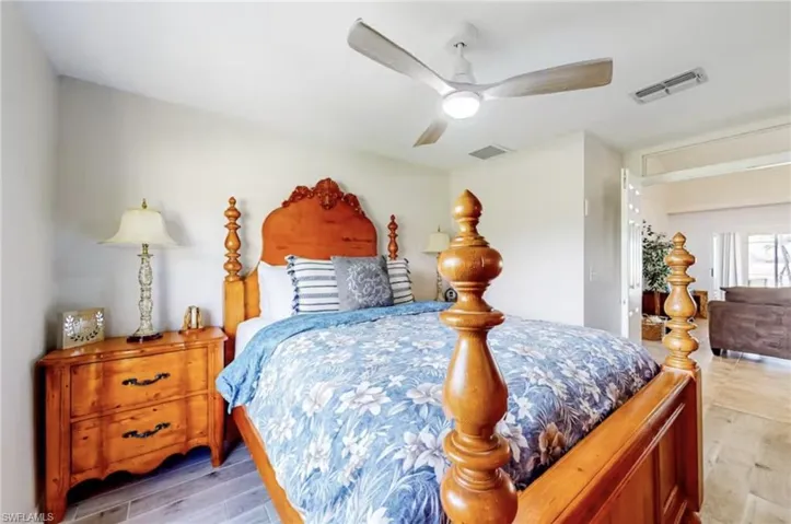 Bedroom featuring wood-finish flooring, a ceiling fan with integrated lighting, and a doorway opening to another interior space