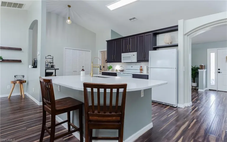 Kitchen with arched walkways, white appliances, open shelves, dark wood-style flooring, and a breakfast bar area