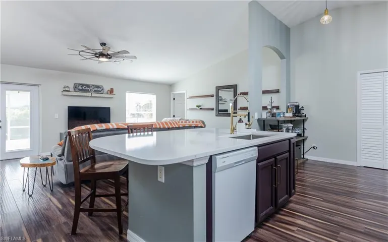 Kitchen with lofted ceiling, dark wood finished floors, white dishwasher, open floor plan, and a kitchen island with sink