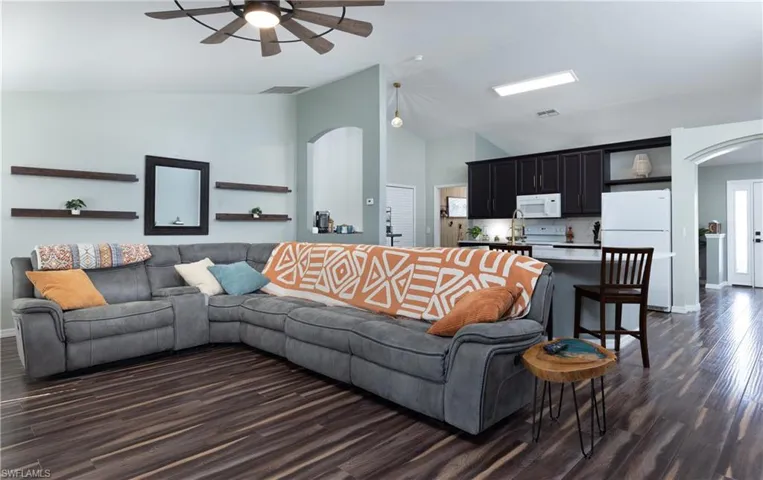 Living room featuring arched walkways, vaulted ceiling, dark wood-style flooring, and a ceiling fan