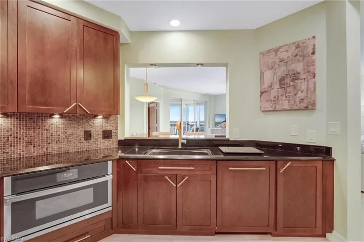 Kitchen featuring stainless steel oven, wood cabinets, decorative backsplash and dark stone counters.