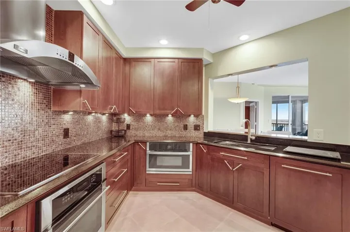 Kitchen featuring wall chimney exhaust hood, stainless steel oven, black electric stovetop, decorative backsplash, and recessed lighting