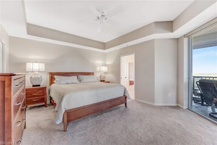 Primary Bedroom featuring access to lanai, a tray ceiling, and light carpet