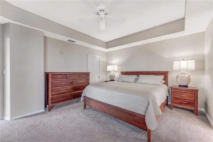Primary Bedroom with a ceiling fan, light carpet, and a tray ceiling