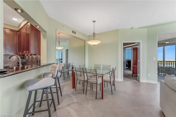 Breakfast bar with pass through to kitchen and Dining space featuring recessed lighting and light tile floors with a mirrored wall.