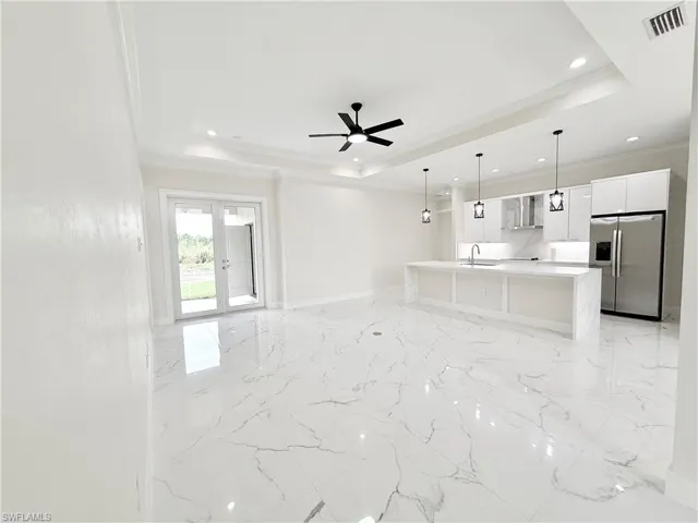Unfurnished living room featuring a raised ceiling, light marble finish floors, french doors, ornamental molding, and a ceiling fan