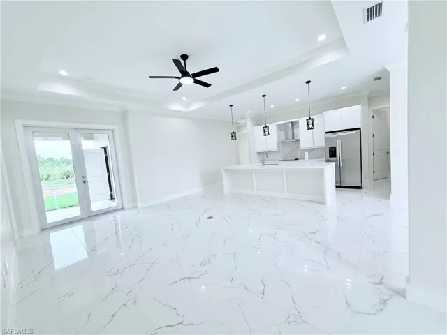 Unfurnished living room featuring a raised ceiling, crown molding, baseboards, recessed lighting, and a ceiling fan