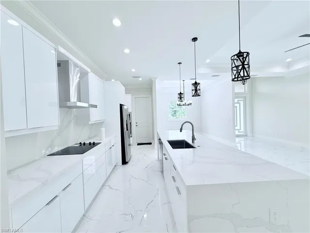 Kitchen featuring modern cabinets, wall chimney exhaust hood, a sink, recessed lighting, and light marble finish floors
