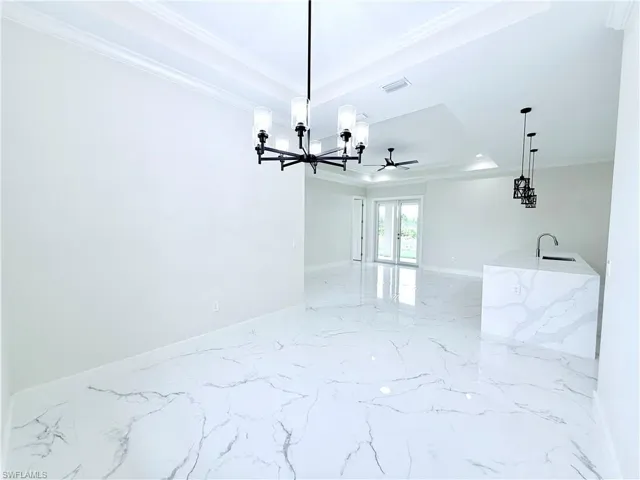 Unfurnished room featuring a raised ceiling, crown molding, a chandelier, light marble finish floors, and baseboards