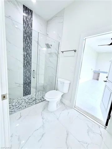 Full bath with a marble finish shower, toilet, marble finish floors, baseboards, and a ceiling fan