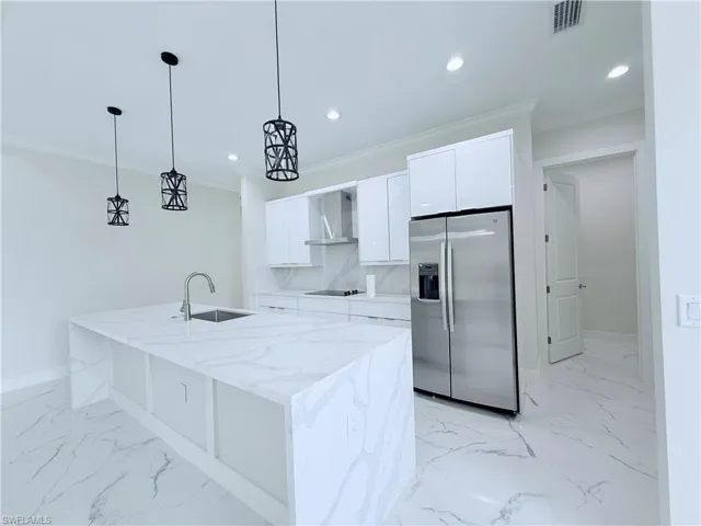 Kitchen with stainless steel refrigerator with ice dispenser, a sink, wall chimney exhaust hood, baseboards, and white cabinetry
