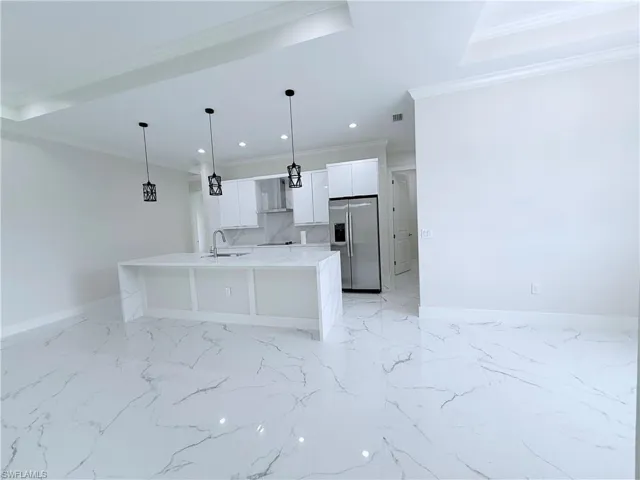 Kitchen featuring stainless steel fridge with ice dispenser, a sink, crown molding, white cabinetry, and baseboards