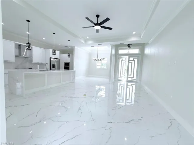 Unfurnished living room featuring ornamental molding, a chandelier, a sink, a tray ceiling, and baseboards