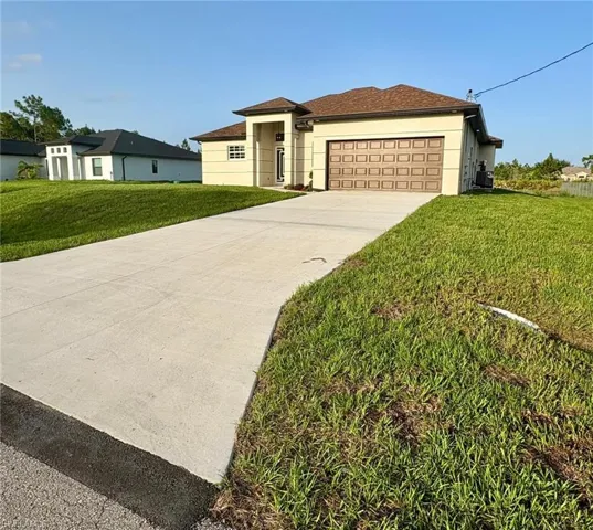 View of front of home with an attached garage, concrete driveway, a front lawn, and stucco siding