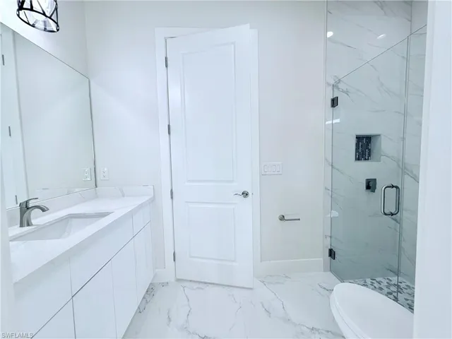 Full bathroom featuring marble finish flooring, a marble finish shower, vanity, toilet, and baseboards