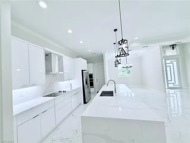 Kitchen with modern cabinets, wall chimney exhaust hood, a sink, a large island with sink, and crown molding
