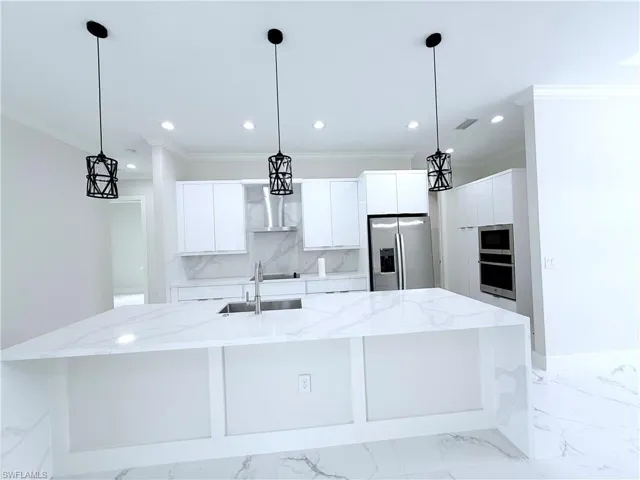 Kitchen with stainless steel refrigerator with ice dispenser, a sink, wall chimney range hood, recessed lighting, and crown molding