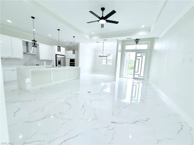 Unfurnished living room featuring ornamental molding, light marble finish floors, a chandelier, recessed lighting, and a sink