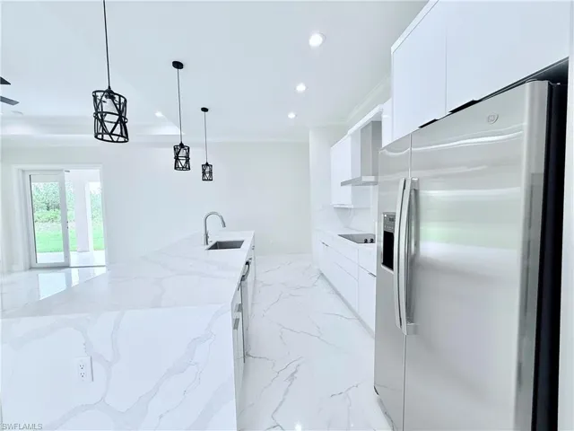 Kitchen featuring stainless steel fridge, modern cabinets, a sink, white cabinets, and recessed lighting