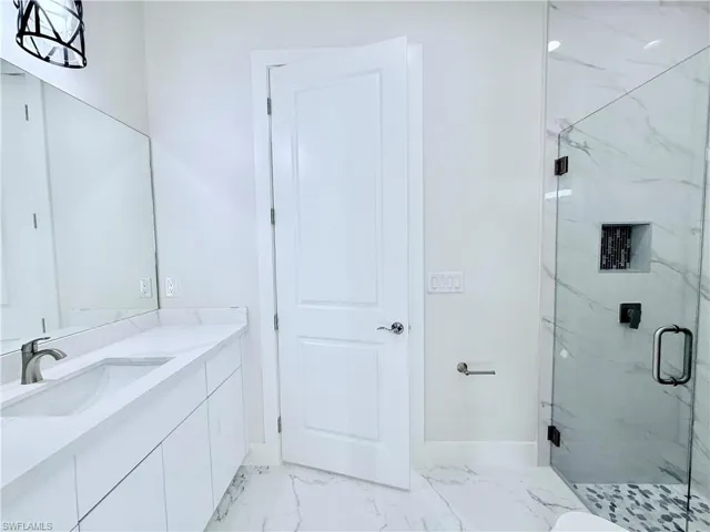 Bathroom featuring a marble finish shower, vanity, marble finish floors, and baseboards