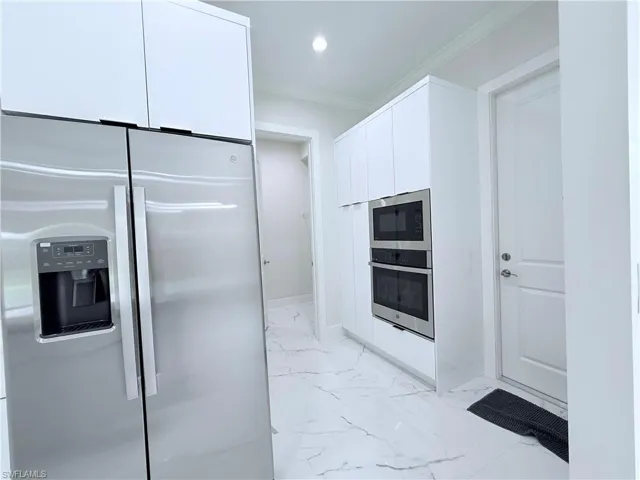 Kitchen featuring appliances with stainless steel finishes, white cabinetry, ornamental molding, light marble finish floors, and recessed lighting
